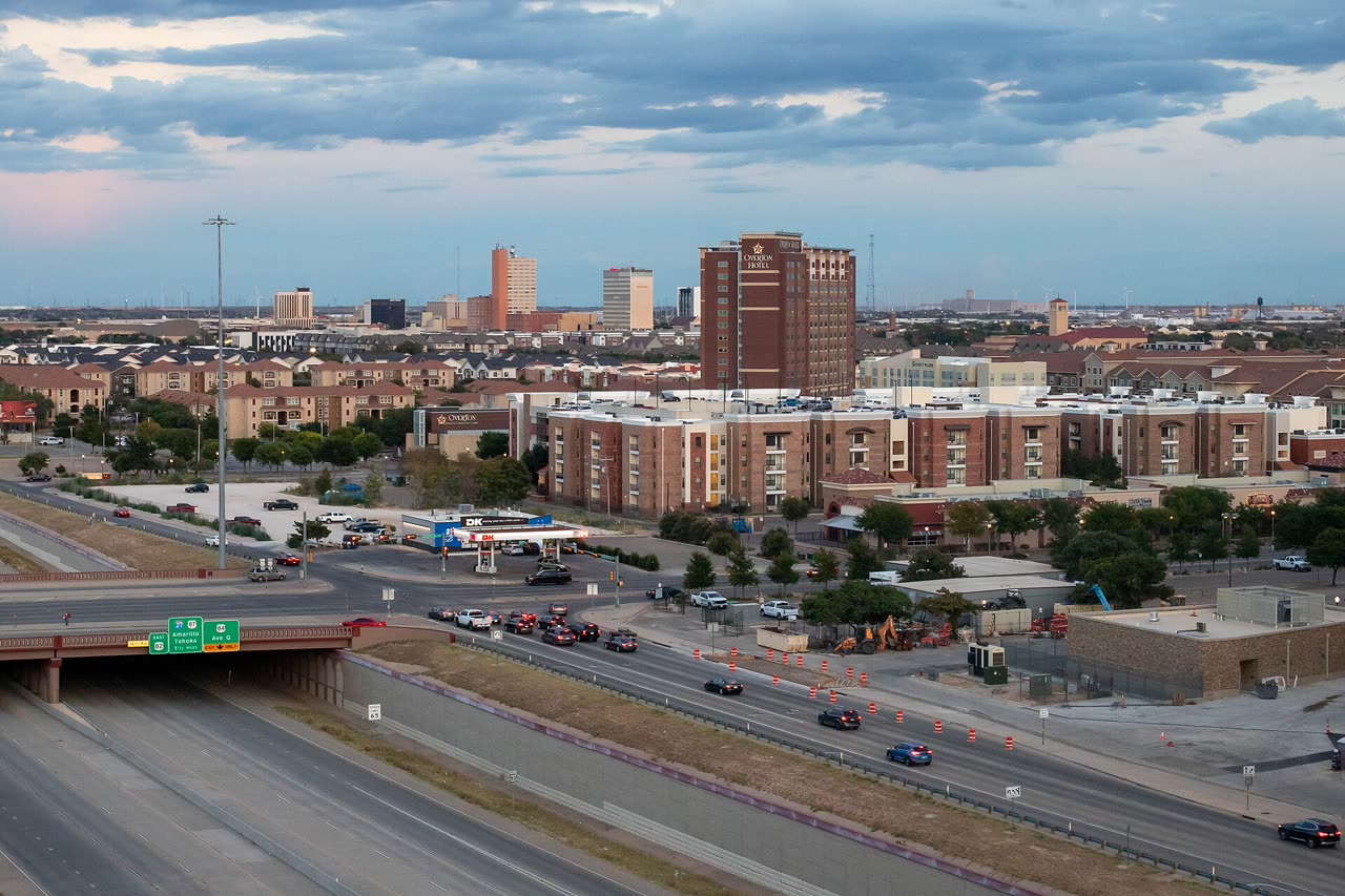 El centro de Lubbock al atardecer bajo un cielo nublado, con una torre de hotel de ladrillo y edificios de apartamentos junto a un paso a desnivel de la autopista